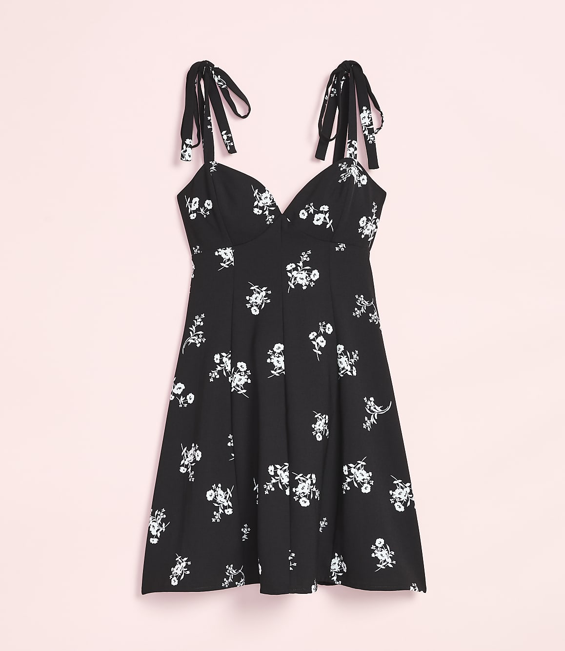 A black floral print dress with tie straps hangs against a soft pink background.