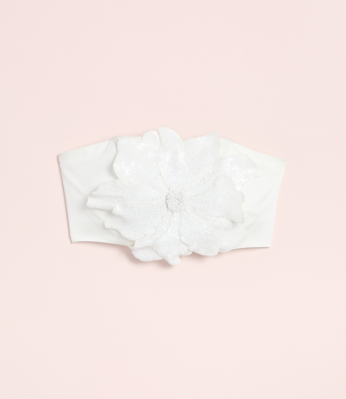 A white fabric headband with a large, ornate flower adorns a soft pink background.