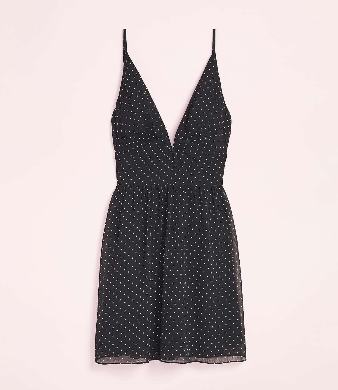 A black polka dot mini dress with thin straps is laid out against a soft pink background.
