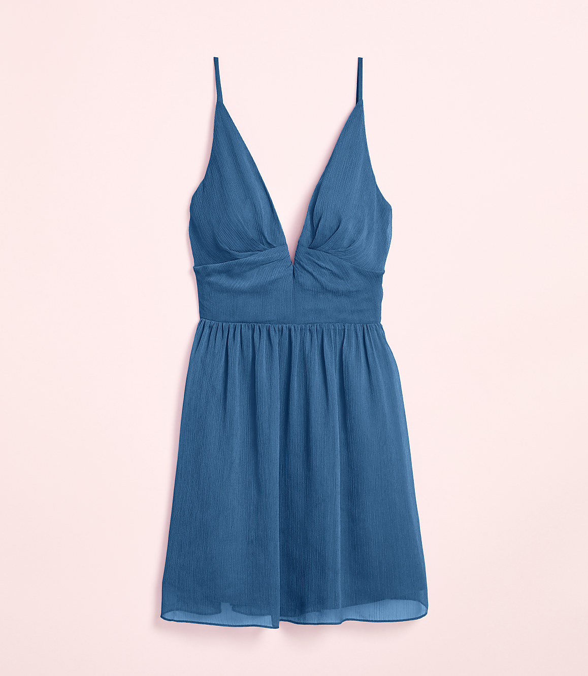 A teal slip dress with a deep V-neckline and spaghetti straps rests against a soft pink background.