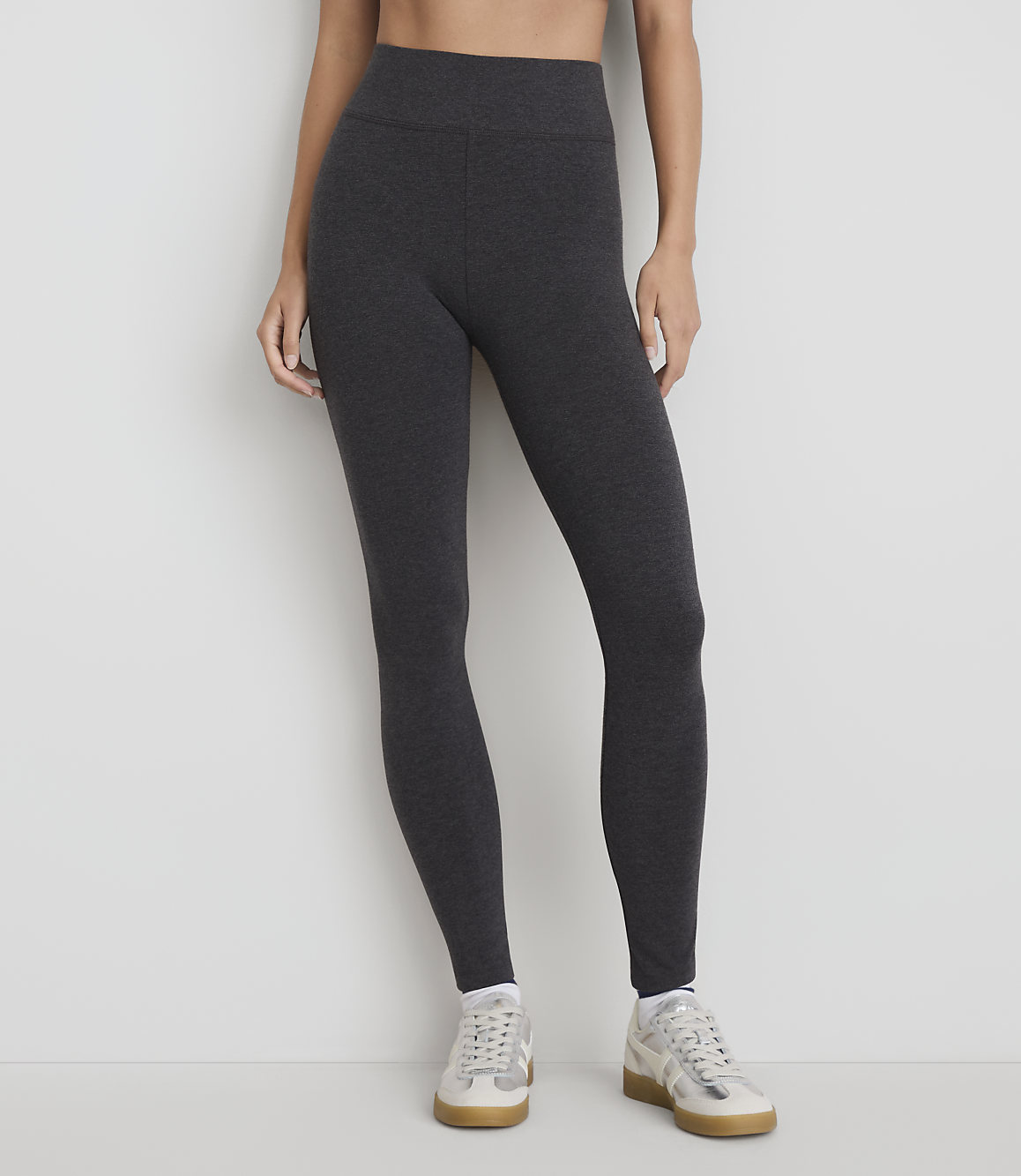 A person stands in dark grey leggings and white sneakers against a plain white background.