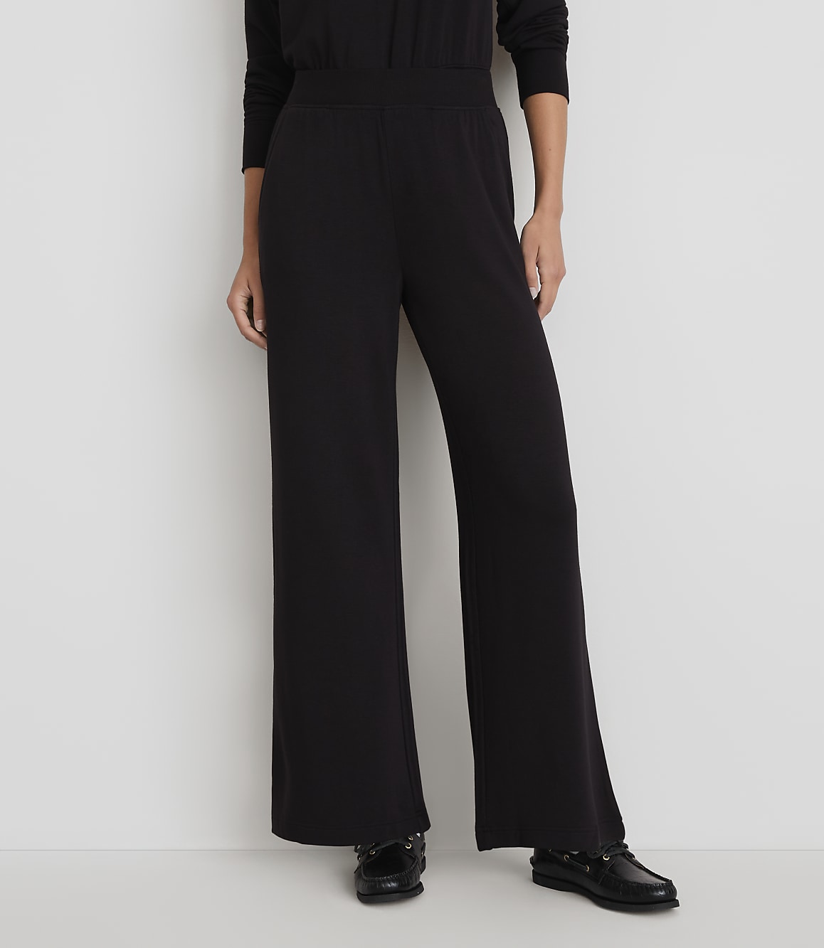 A person stands in wide-legged black pants and black shoes against a plain white background.