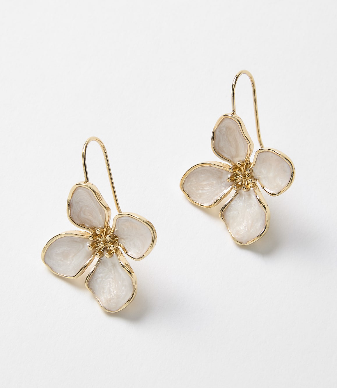 A pair of delicate gold flower-shaped earrings with white enamel petals rest against a plain white background.