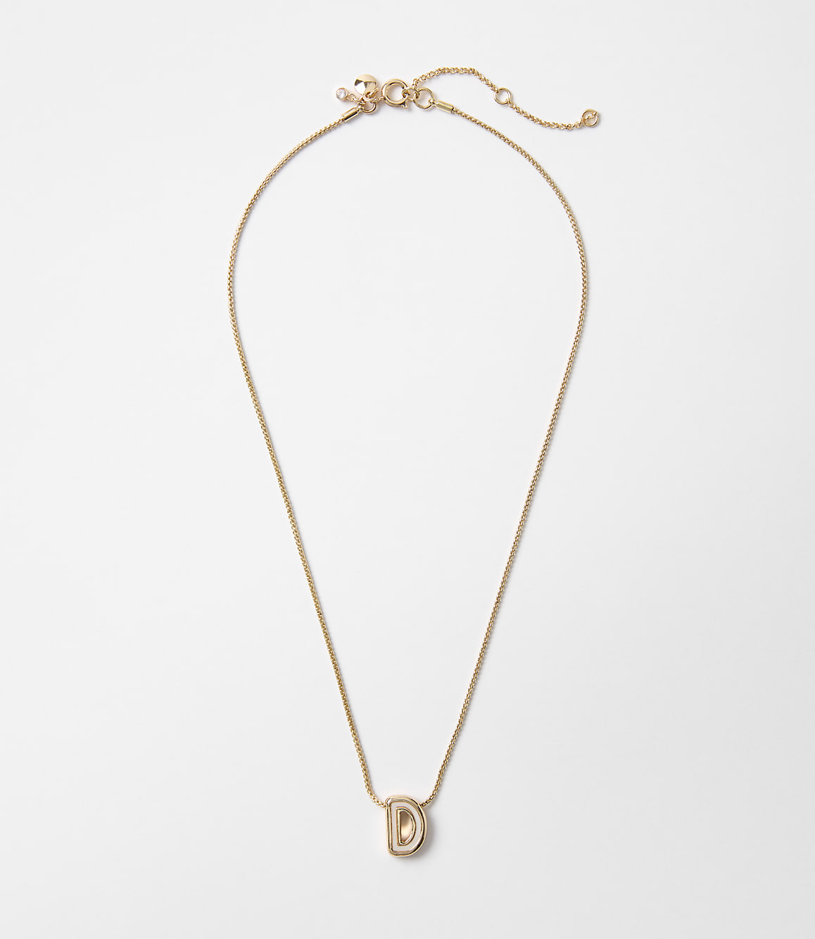 A delicate gold chain necklace with a stylized "D" pendant hangs against a plain white background.