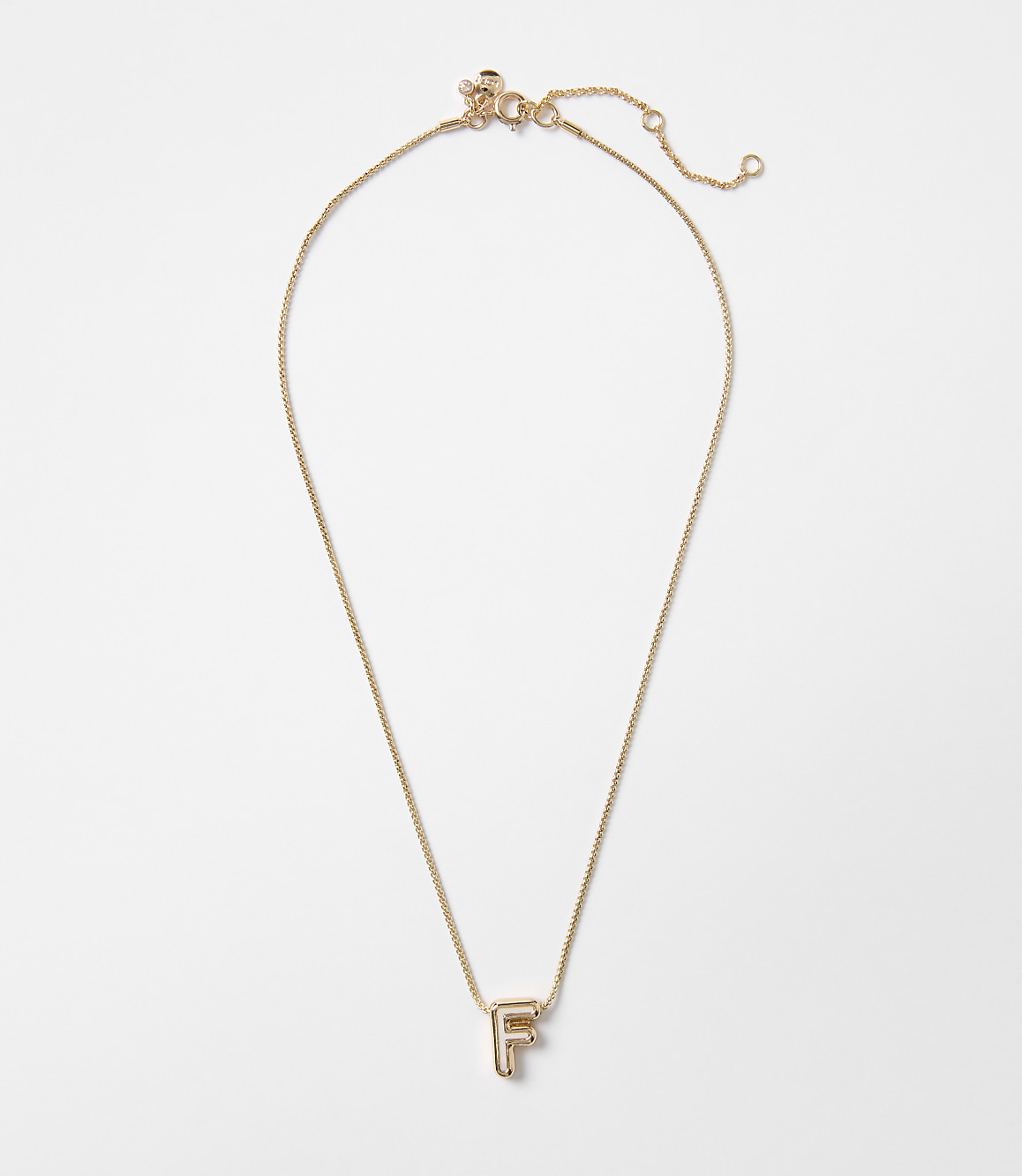 A delicate gold necklace with an "F" initial pendant hangs against a plain white background.