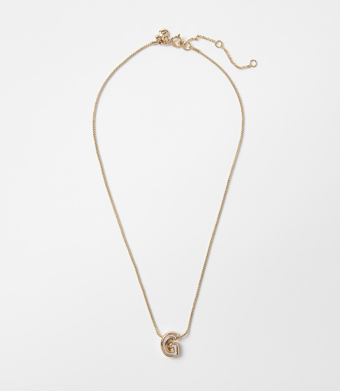 A delicate gold necklace with a "G" charm hangs against a plain white background.
