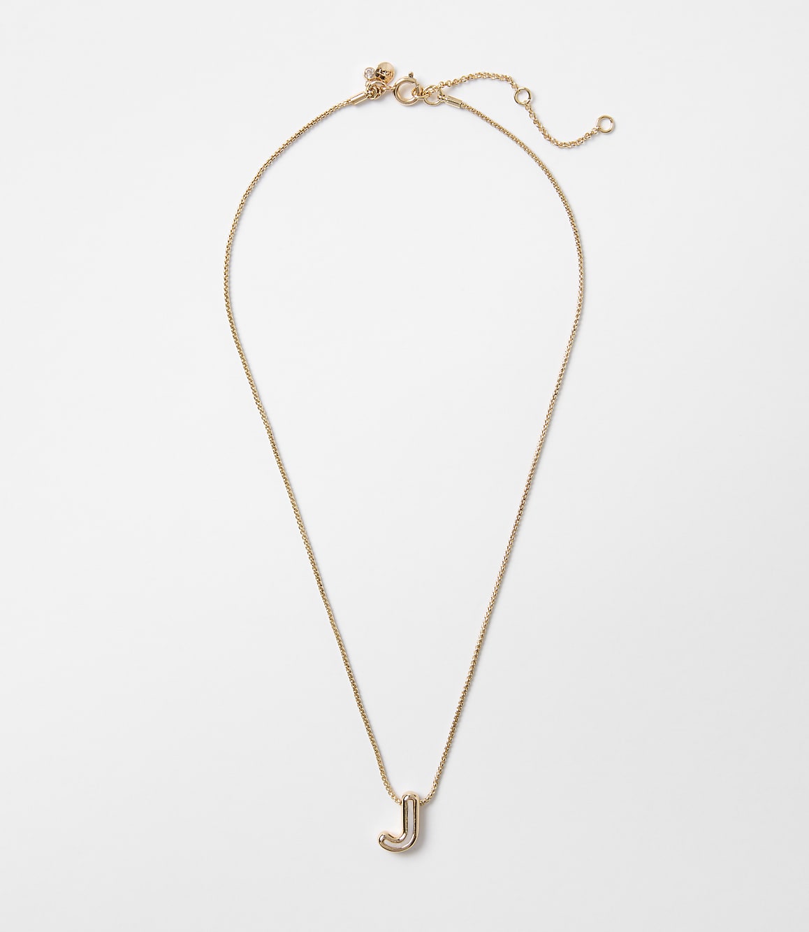 A delicate gold necklace with a stylized "J" pendant hangs against a plain white background.