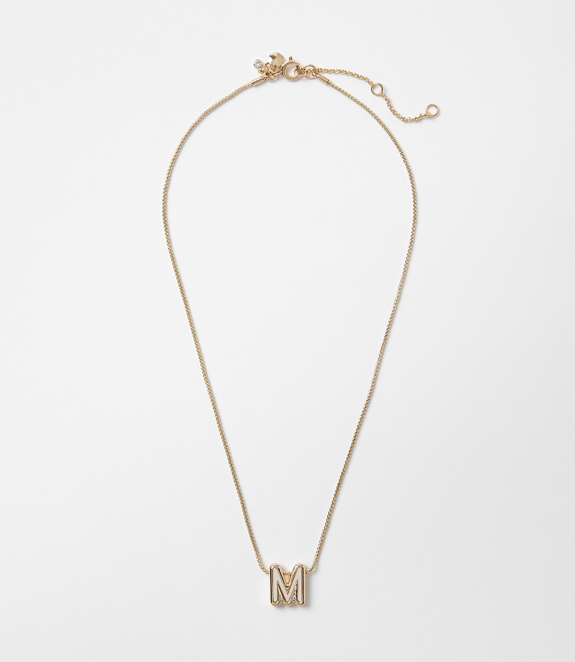 A delicate gold necklace with an "M" pendant rests on a plain white background.