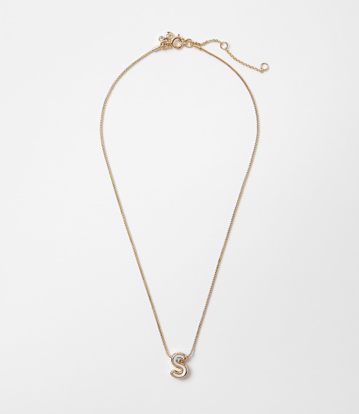 A delicate gold necklace with a sparkling letter "S" pendant hangs against a plain white background.