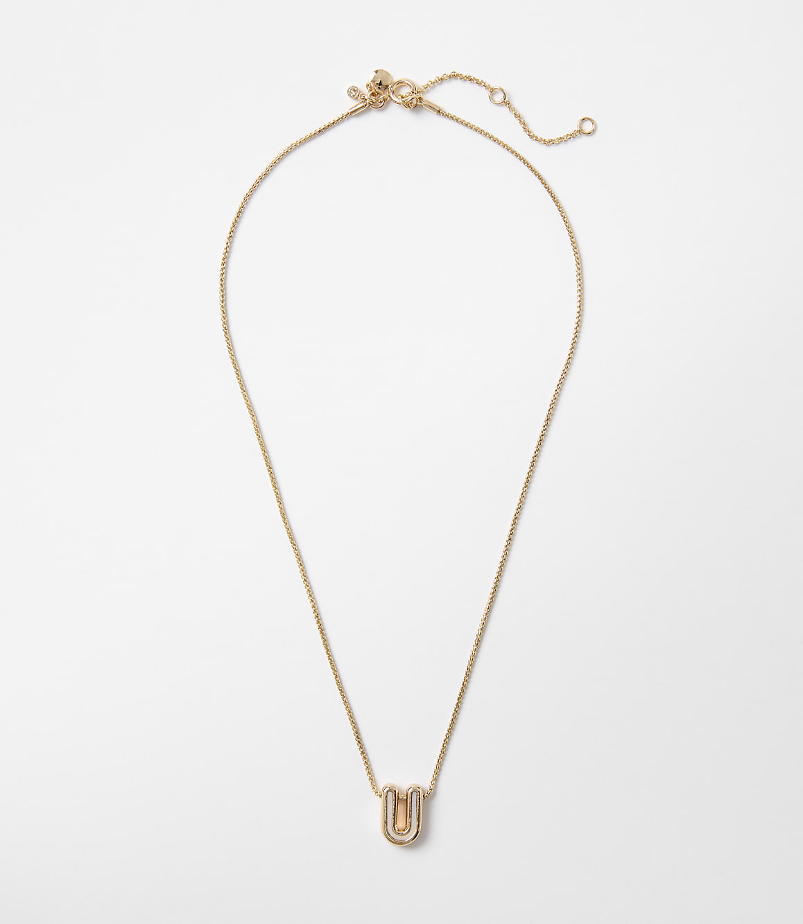 A delicate gold necklace with a stylized "U" pendant rests on a plain white background.