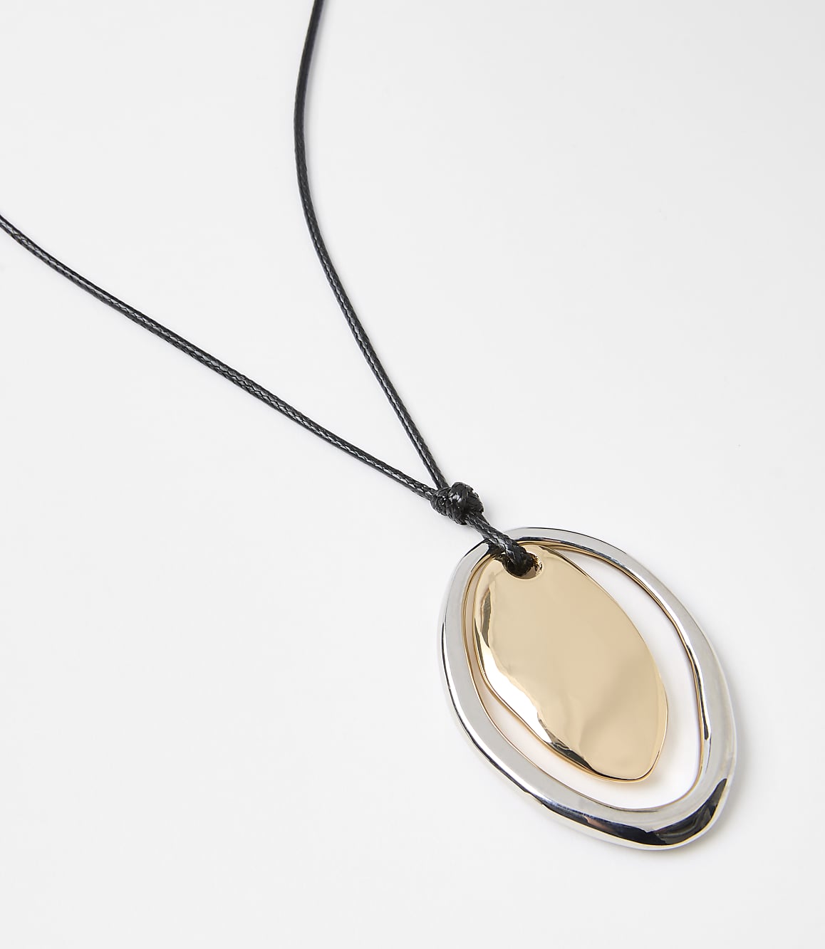 A gold and silver pendant hangs from a black cord against a plain white background.