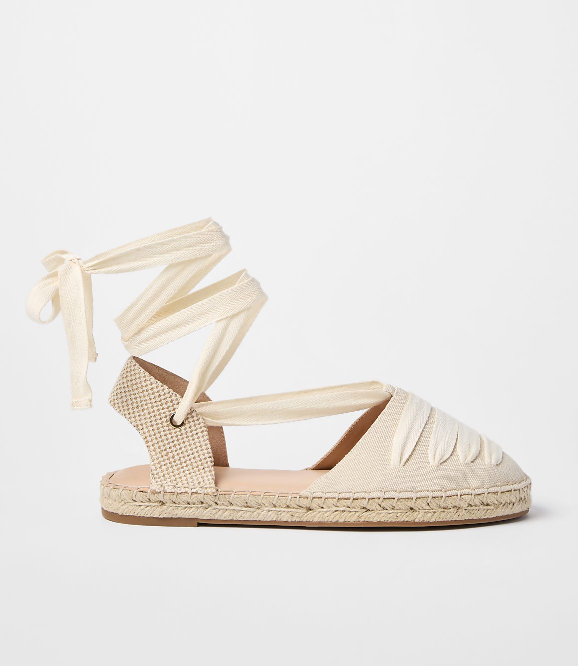 A cream-colored espadrille with ribbon ties is displayed against a plain white background.