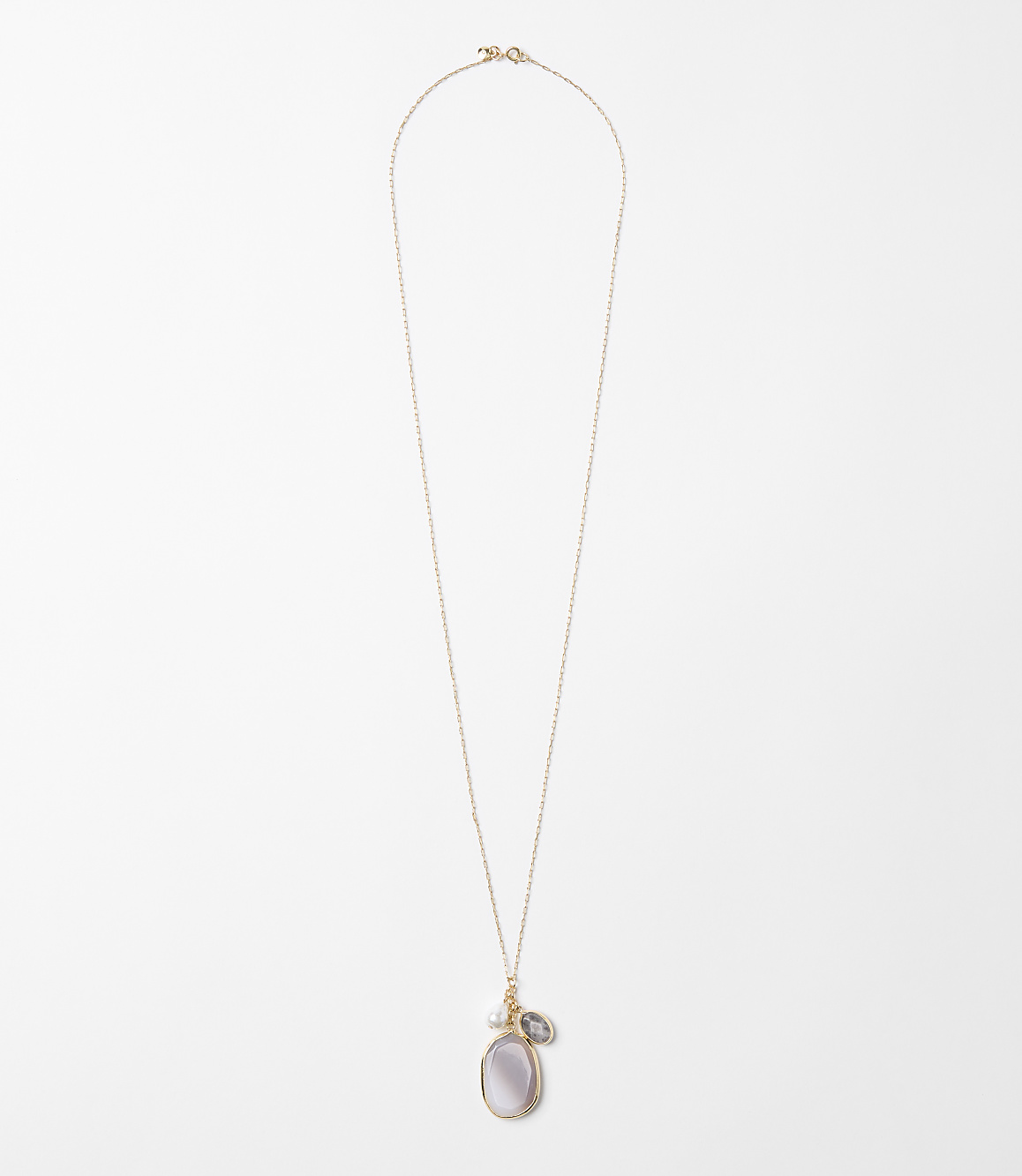A delicate rose gold chain necklace with a pearlescent oval pendant and a small grey stone hangs against a plain white background.