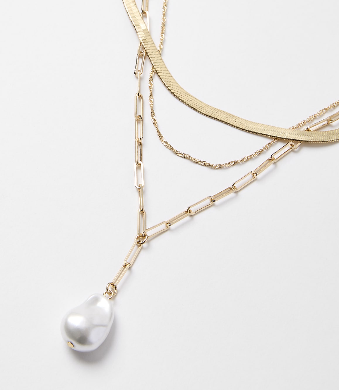 A layered gold necklace with a baroque pearl pendant hangs against a plain white background.