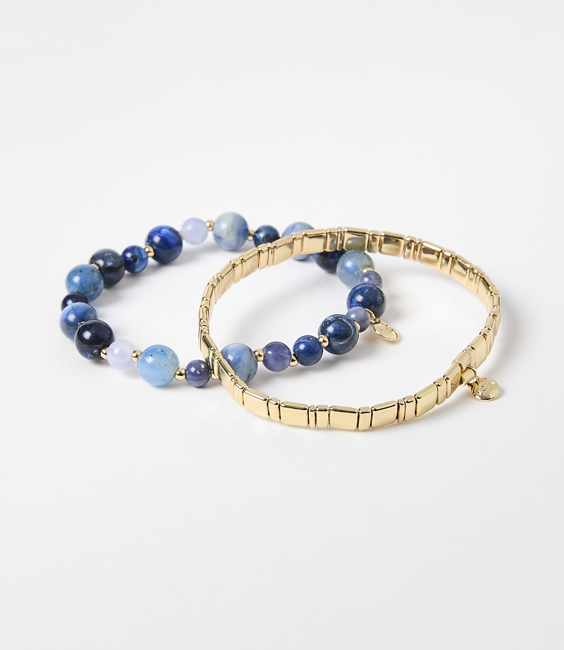 Two bracelets, one with blue beads and the other a gold chain, rest on a plain white background.