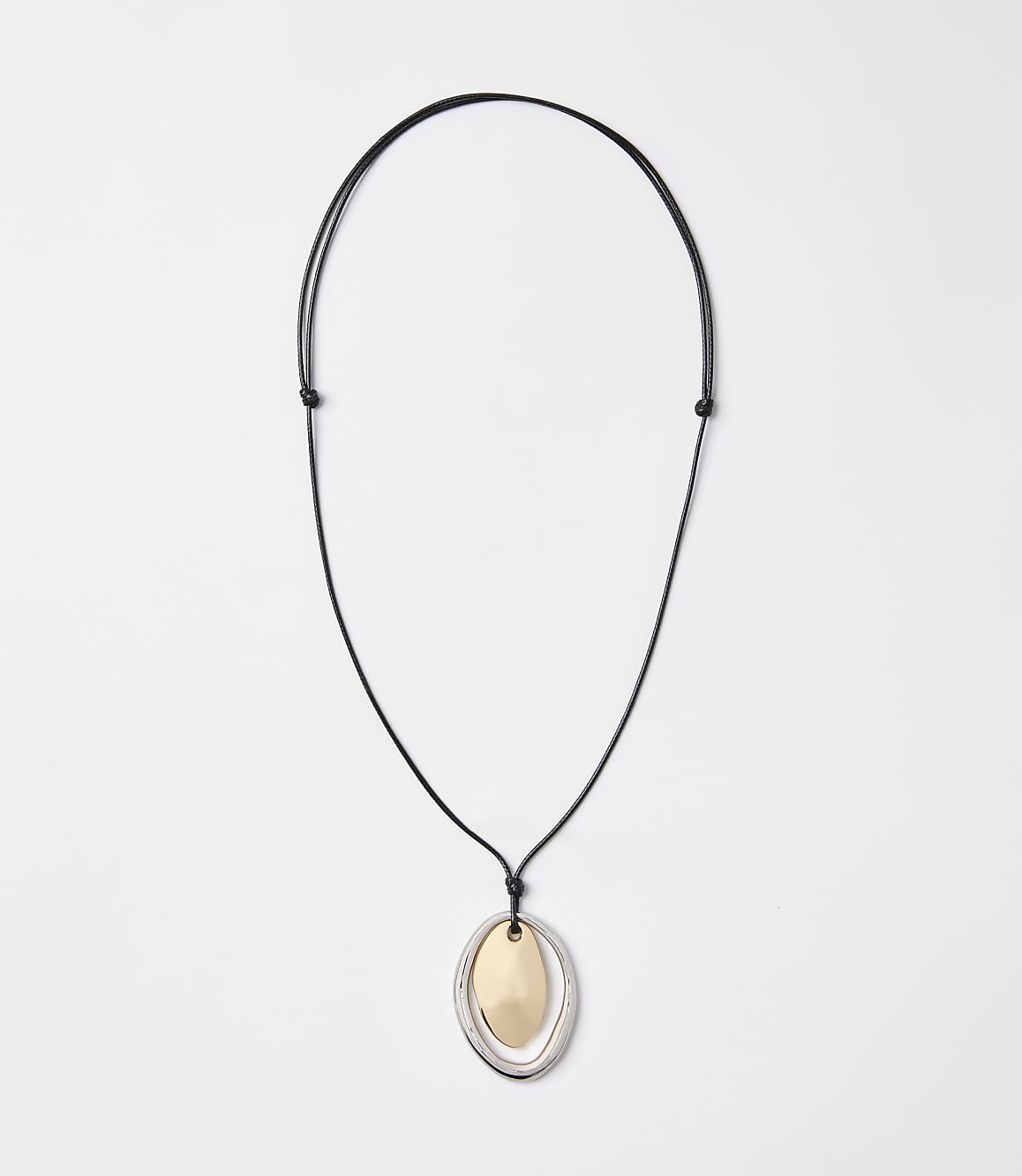A black cord necklace with a layered oval pendant of gold and silver hangs against a plain white background.