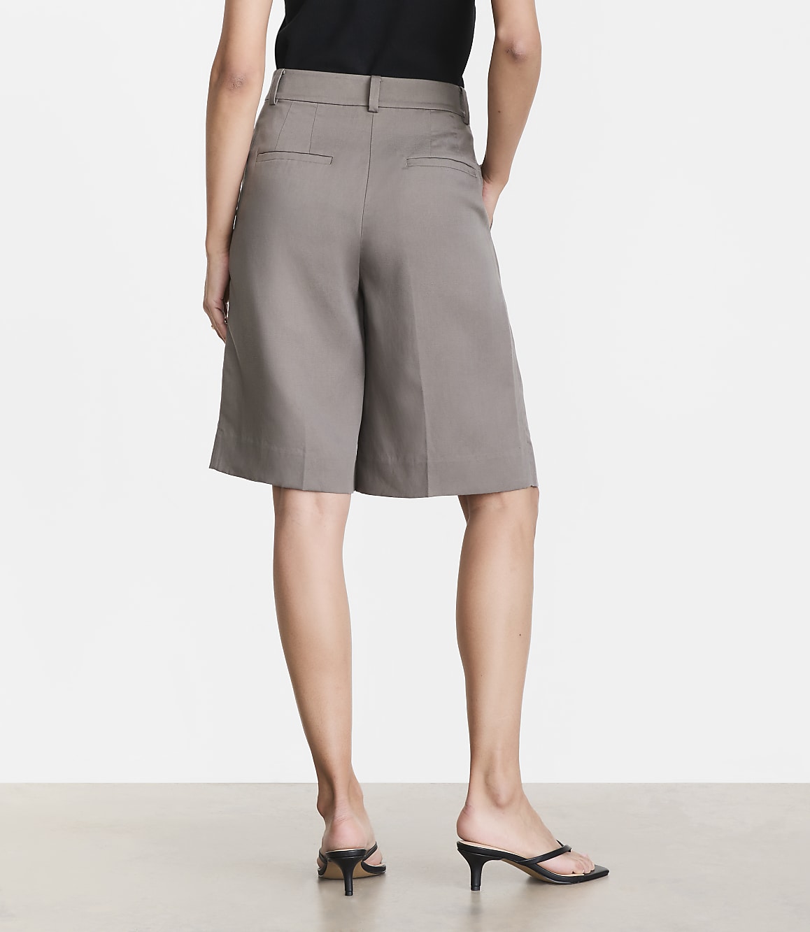 A person wearing grey culottes and black kitten heels stands against a plain grey background.