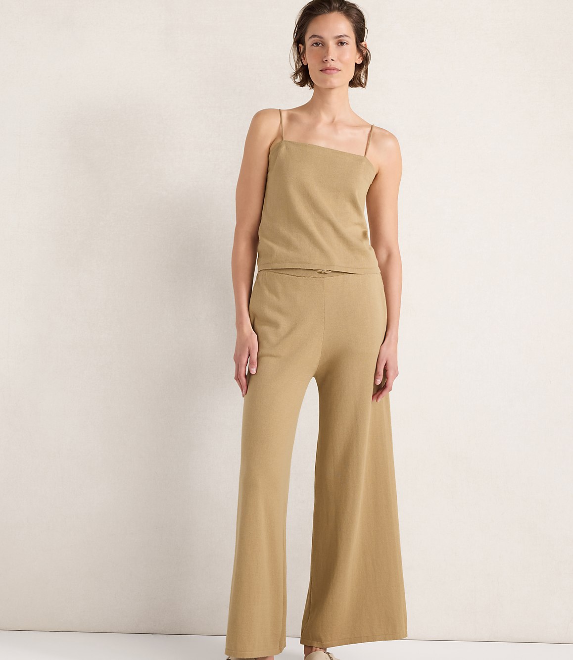A woman in a tan knit camisole and wide-leg pants stands against a plain, light-colored background.