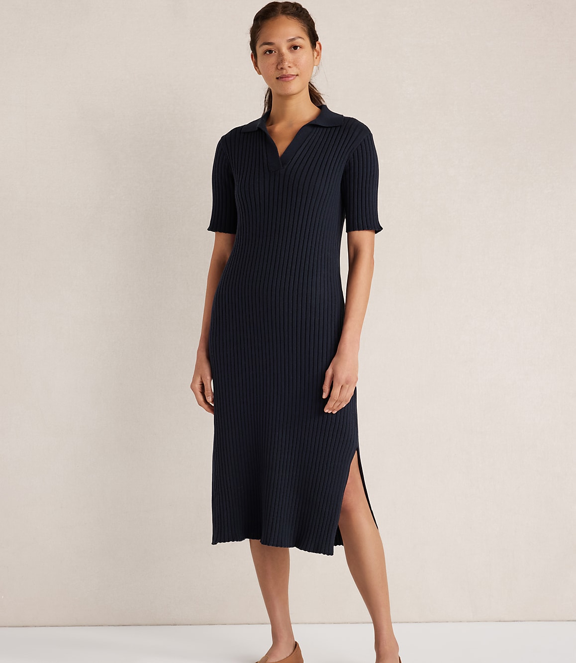 A woman in a navy blue ribbed knit polo dress stands against a plain, light-colored background.