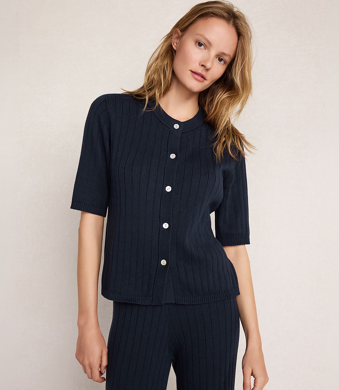 A woman in a navy ribbed cardigan and matching pants stands against a plain, light-colored background.