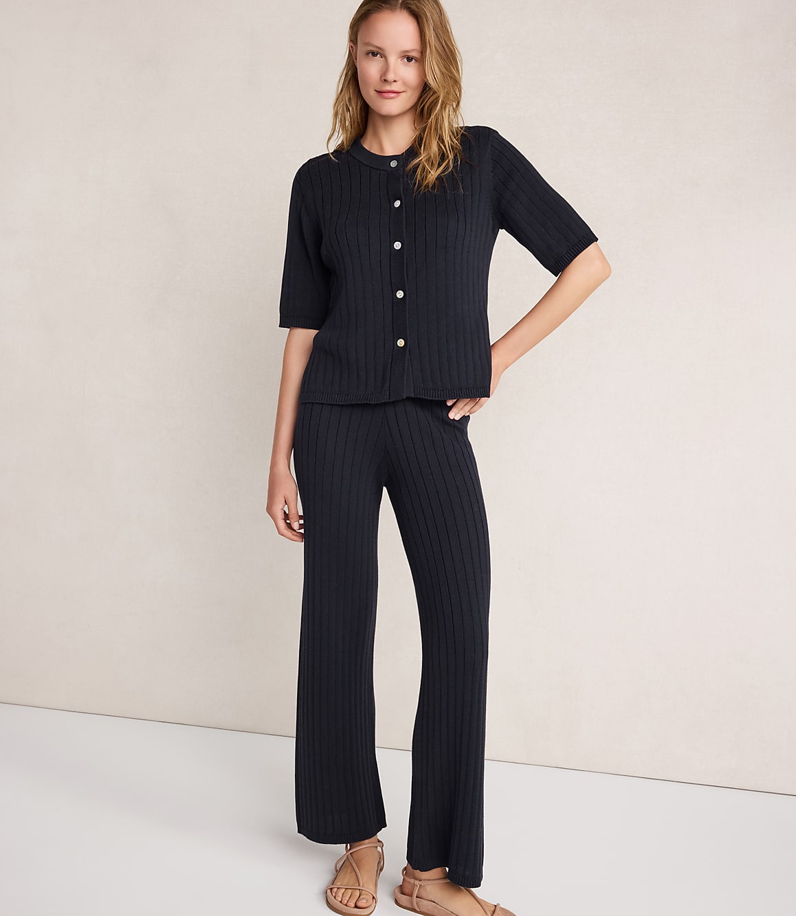A woman in a navy ribbed knit set stands against a textured cream background.