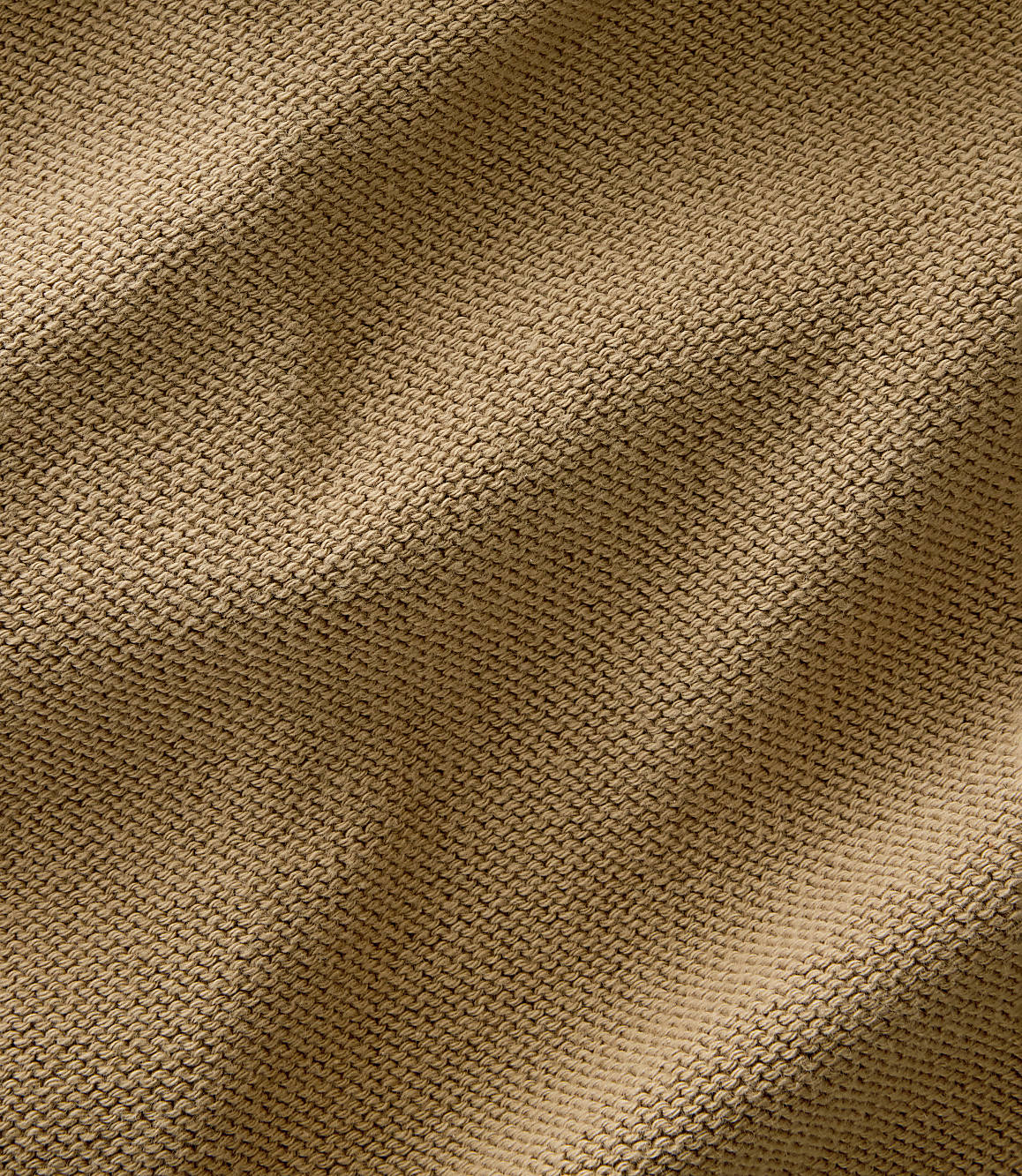 A close-up view of a textured, tan knitted fabric fills the frame, with soft folds and shadows creating depth.