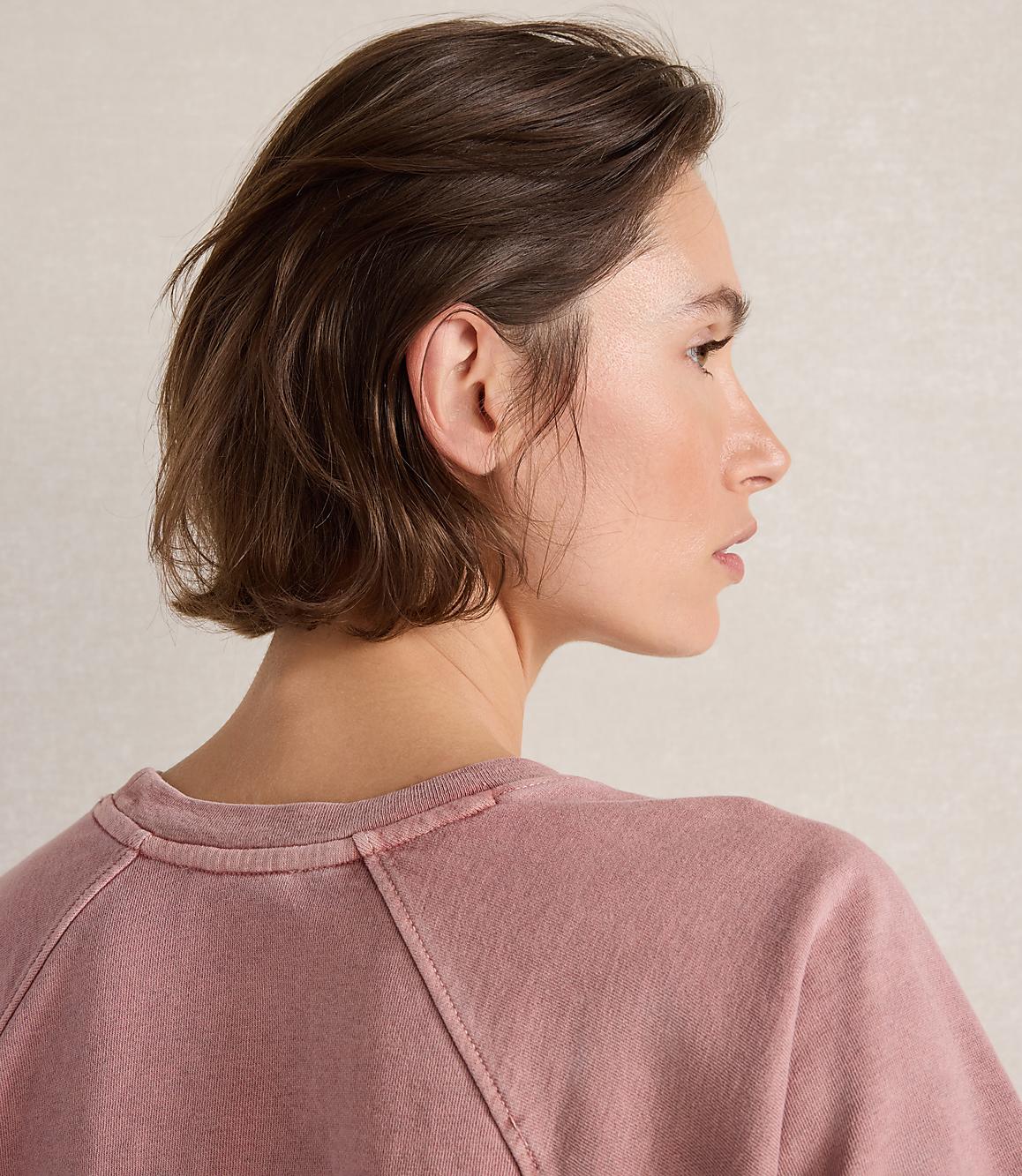 A woman with short brown hair in a pink sweatshirt is shown in profile against a textured, light-colored background.