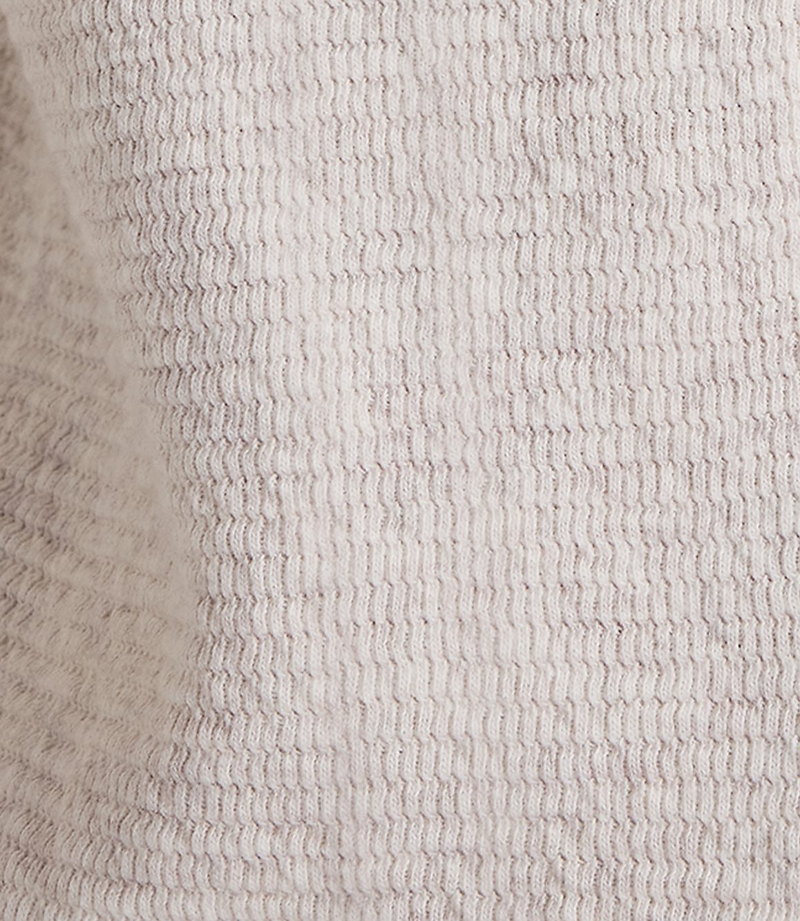 A close-up of a textured, light gray fabric with a subtle wave pattern fills the frame, with soft shadows and highlights creating depth.