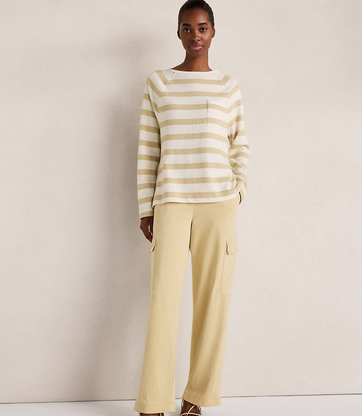 A woman in a striped sweater and yellow cargo pants stands against a plain, light-colored background.