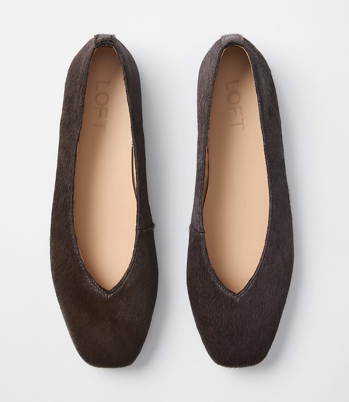 A pair of dark brown, textured ballet flats with a light tan interior and a white background.