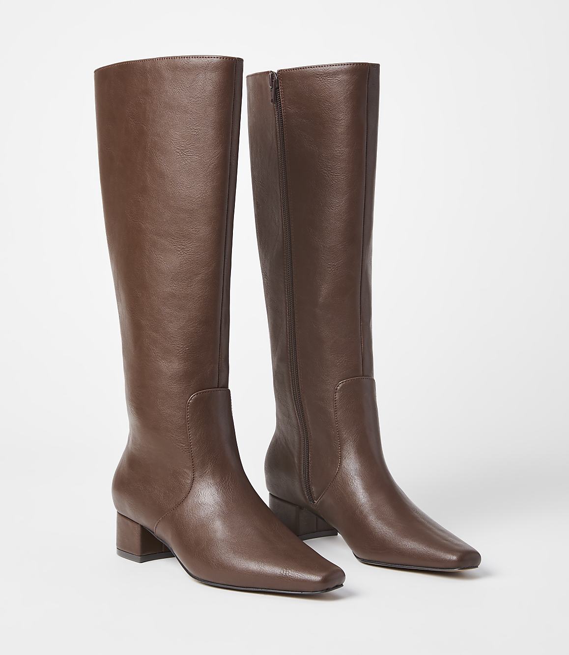 A pair of brown leather knee-high boots with block heels stand on a white surface against a plain white background.