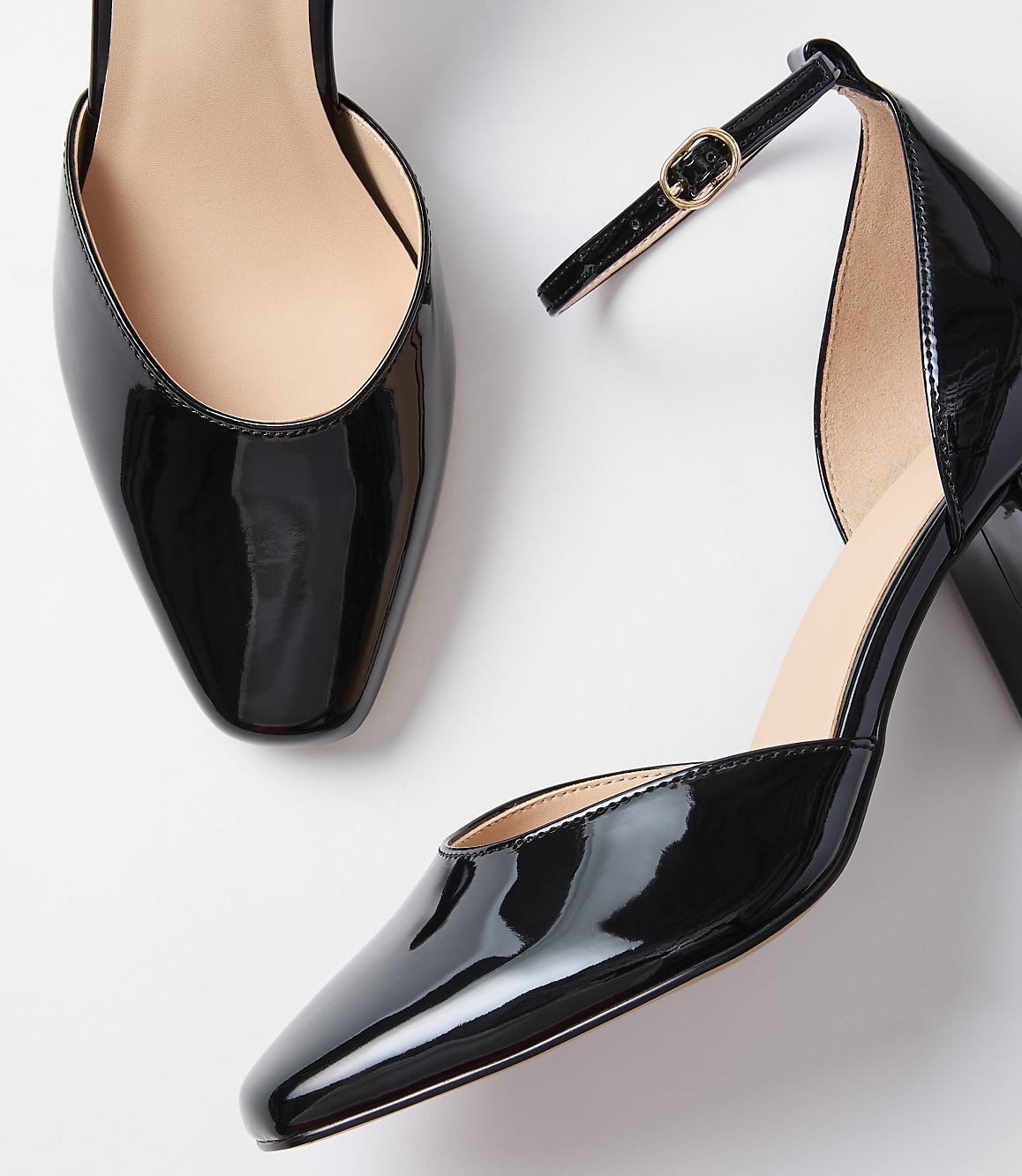 Two glossy black patent leather heels with ankle straps rest on a plain white background.