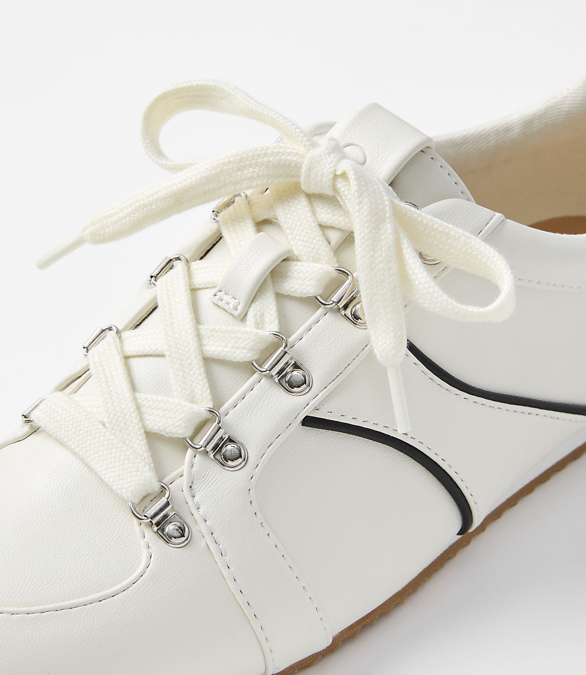 A white sneaker with cream laces is shown in close-up against a plain white background.