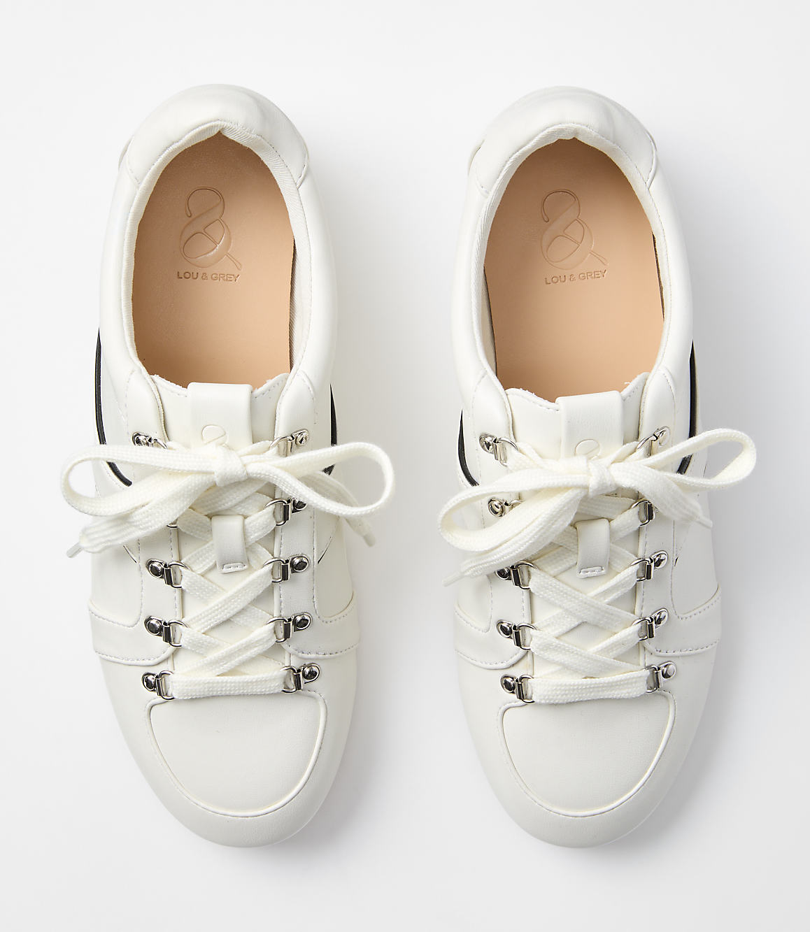 A pair of white leather sneakers with cream laces are laid out on a plain white background.