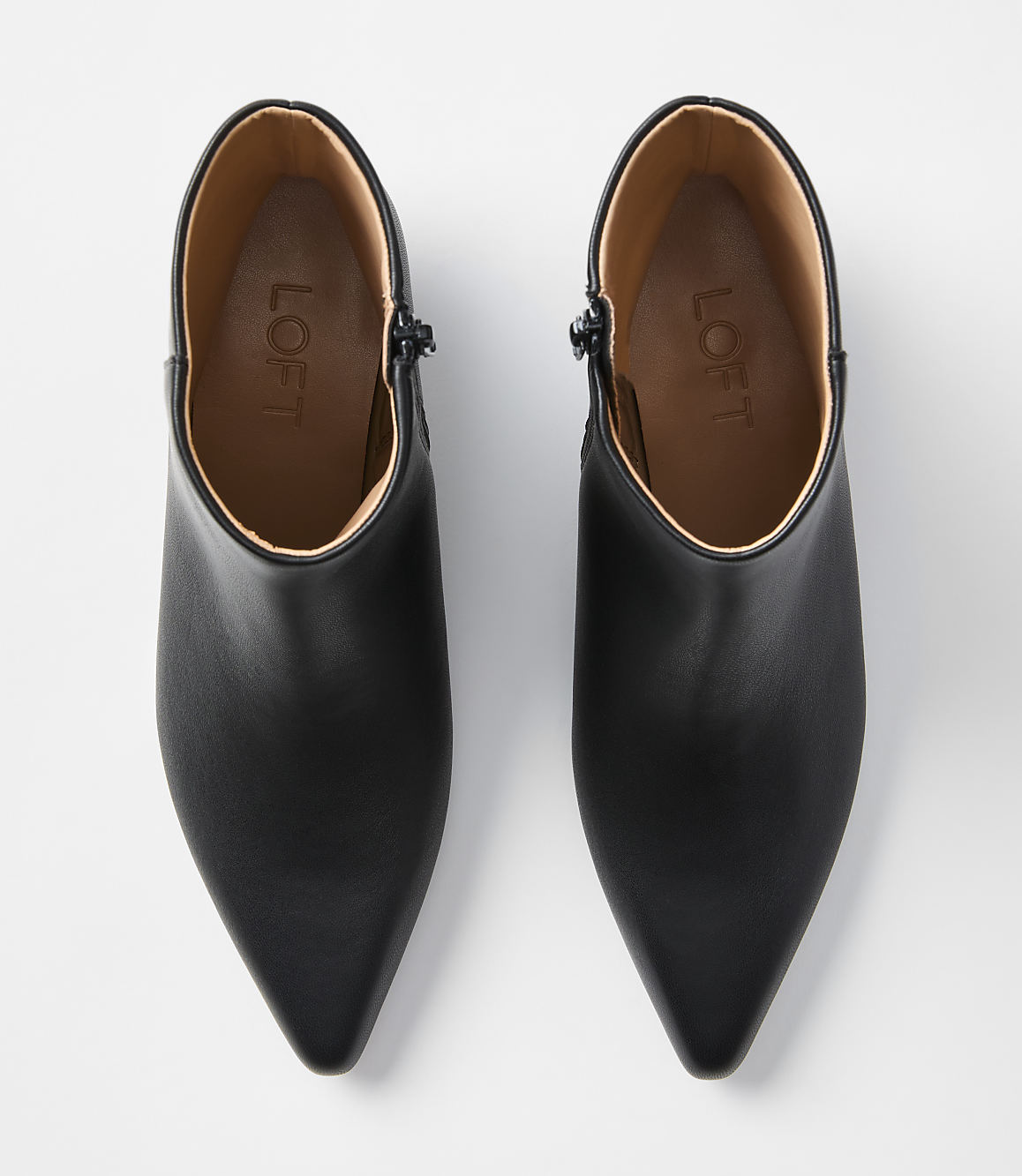 A pair of black, pointed-toe ankle boots with zippers are laid out on a plain white background.