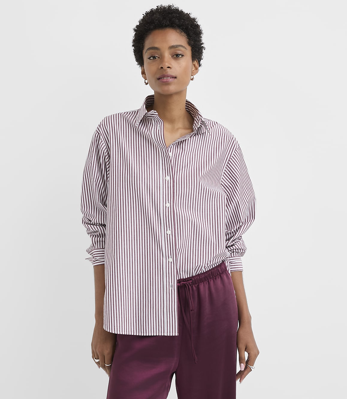 A woman in a striped shirt and satin pants stands against a plain white background.