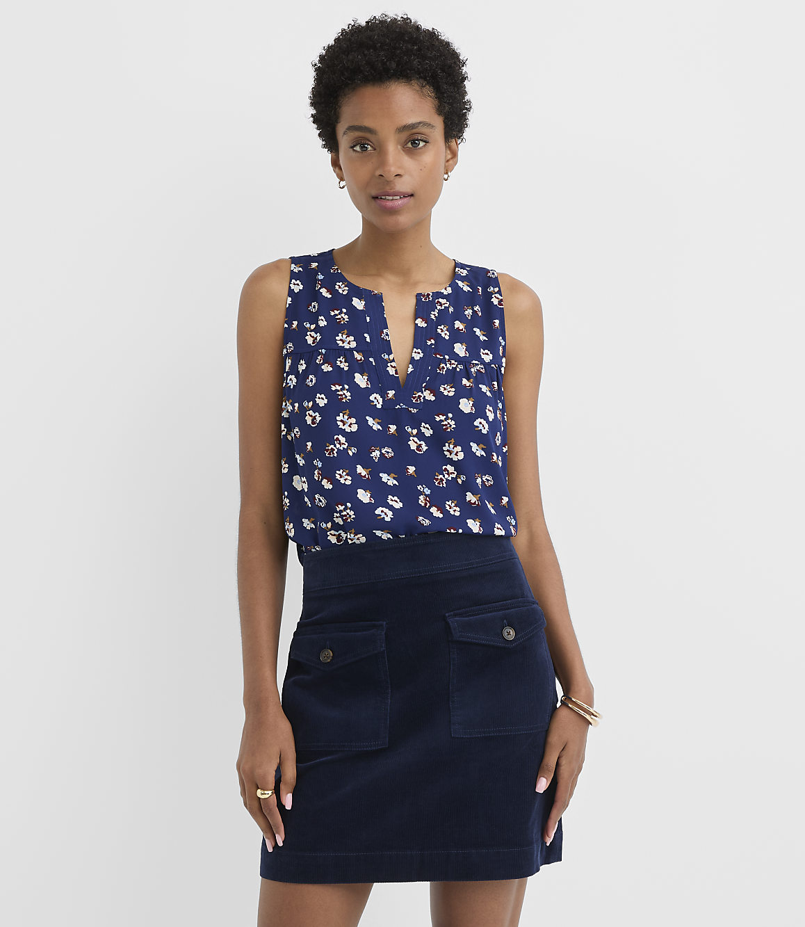 A woman in a floral top and navy corduroy skirt stands against a plain white background.