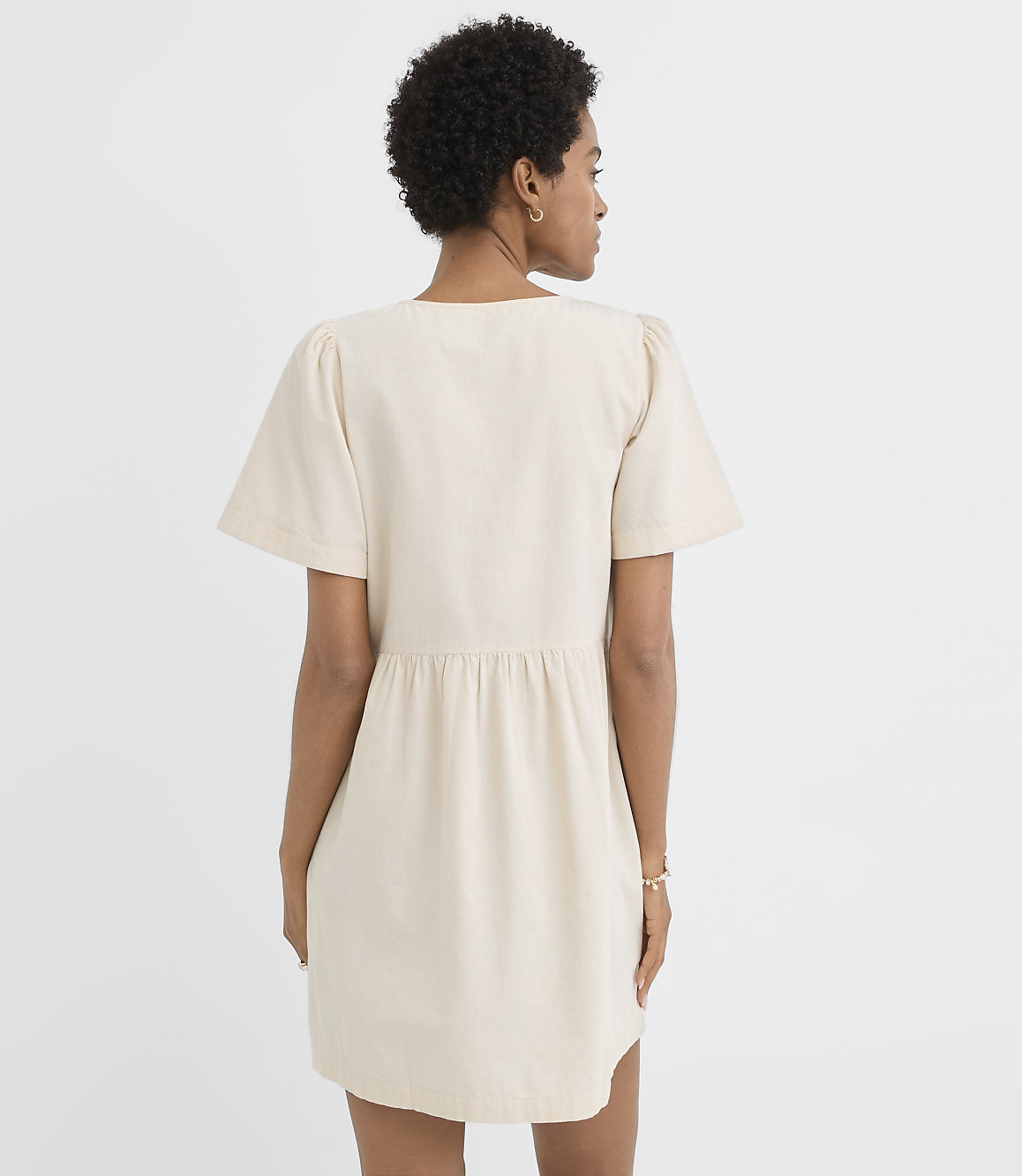A woman in a cream-colored dress stands against a plain white background.
