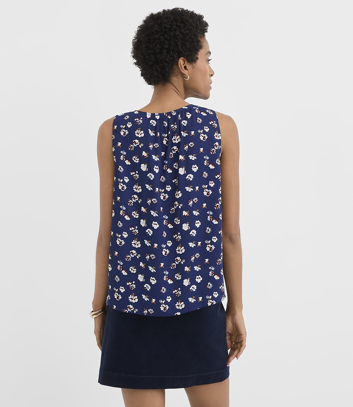A woman in a floral print top and dark skirt stands against a plain white background.