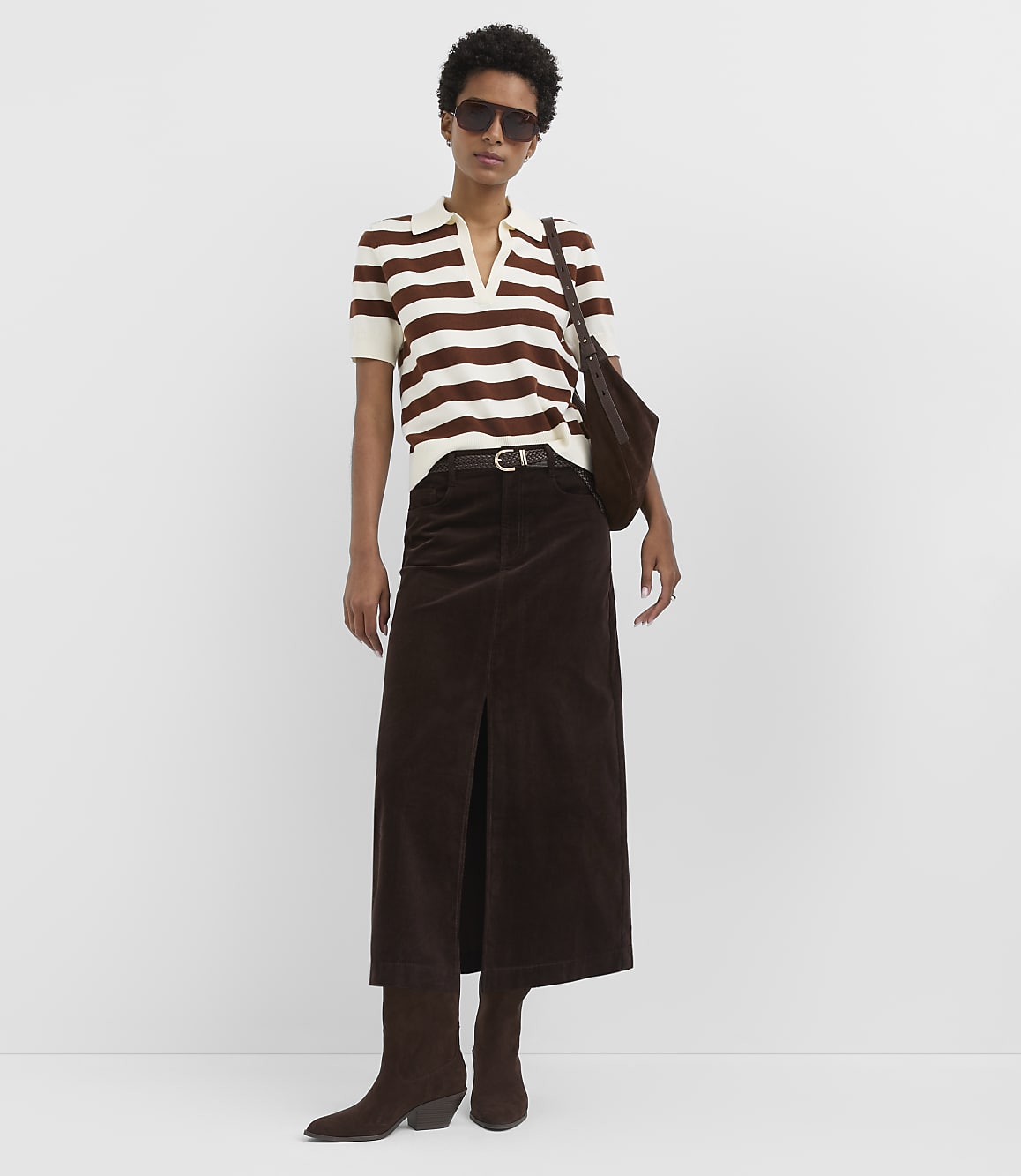 A woman in a striped shirt and brown skirt stands against a plain white background.