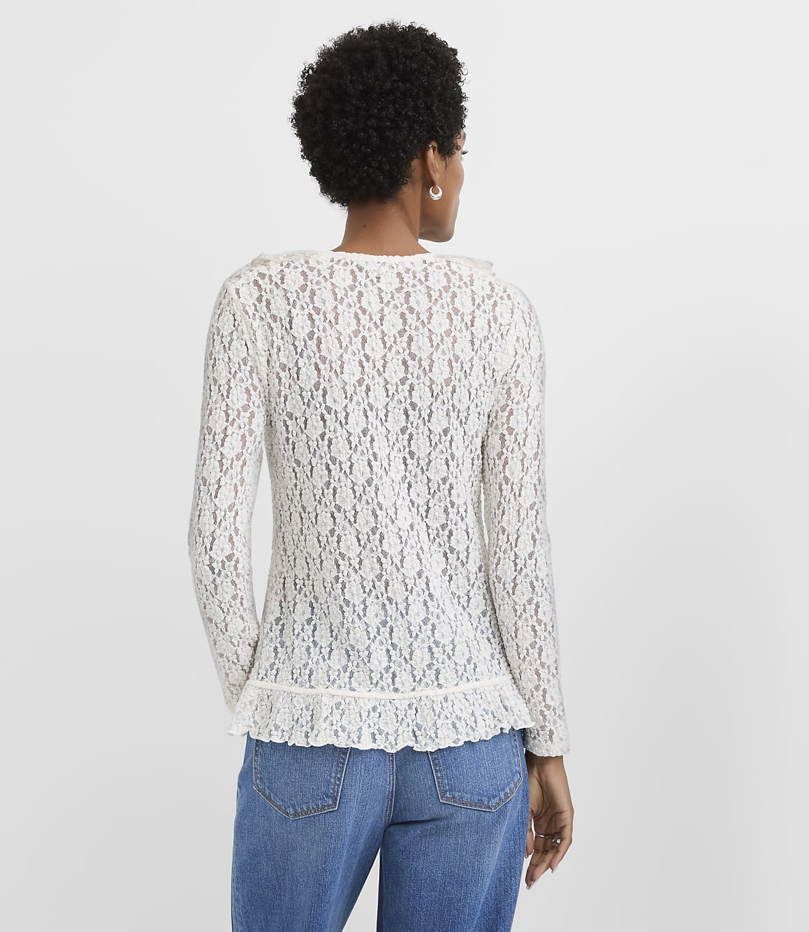 A woman in a white lace top and blue jeans stands against a plain white background.
