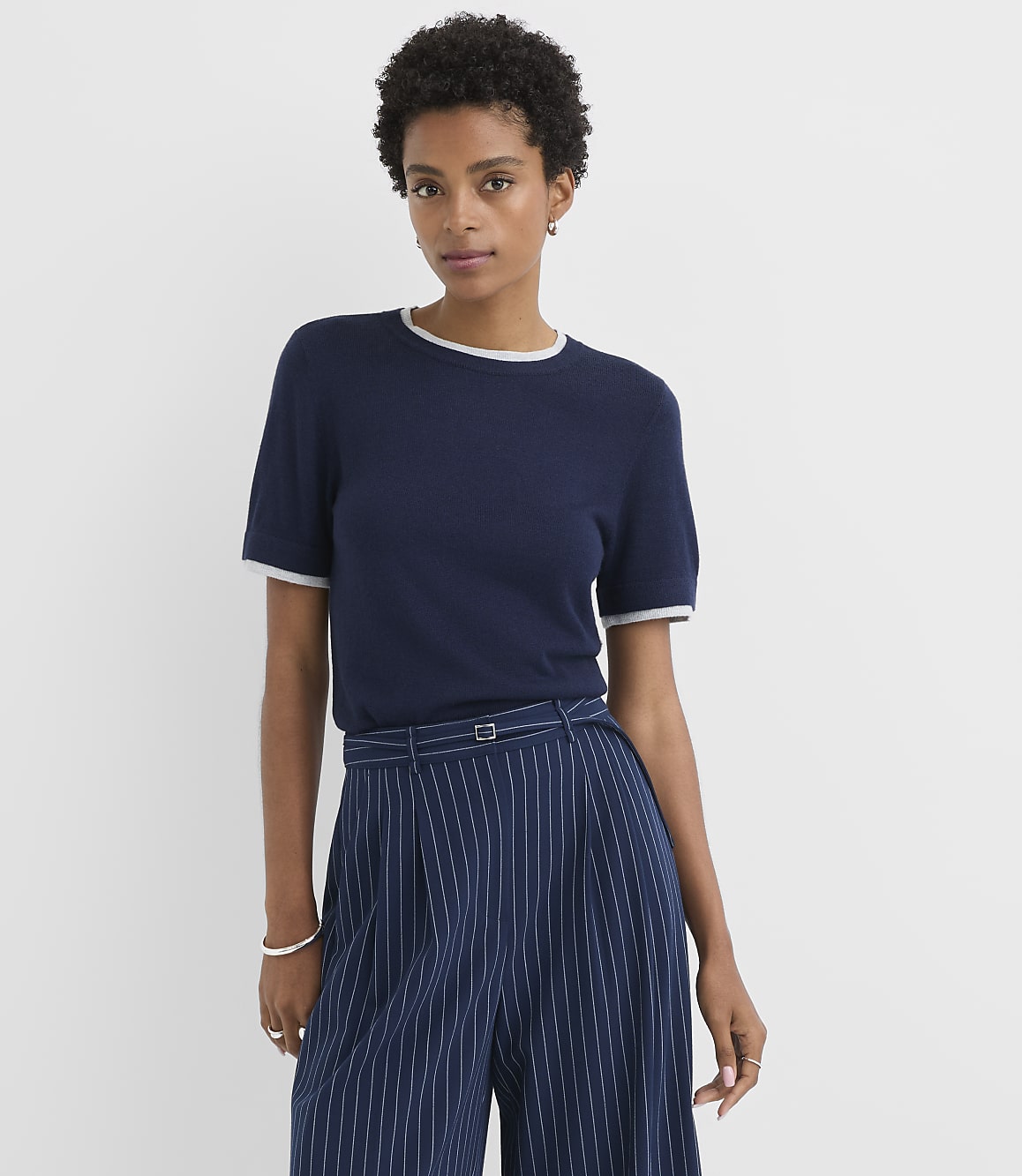 A woman in a navy blue t-shirt and pinstripe pants stands against a plain white background.