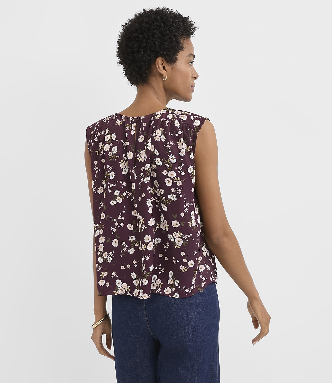 A woman in a floral top and jeans stands against a plain white background.