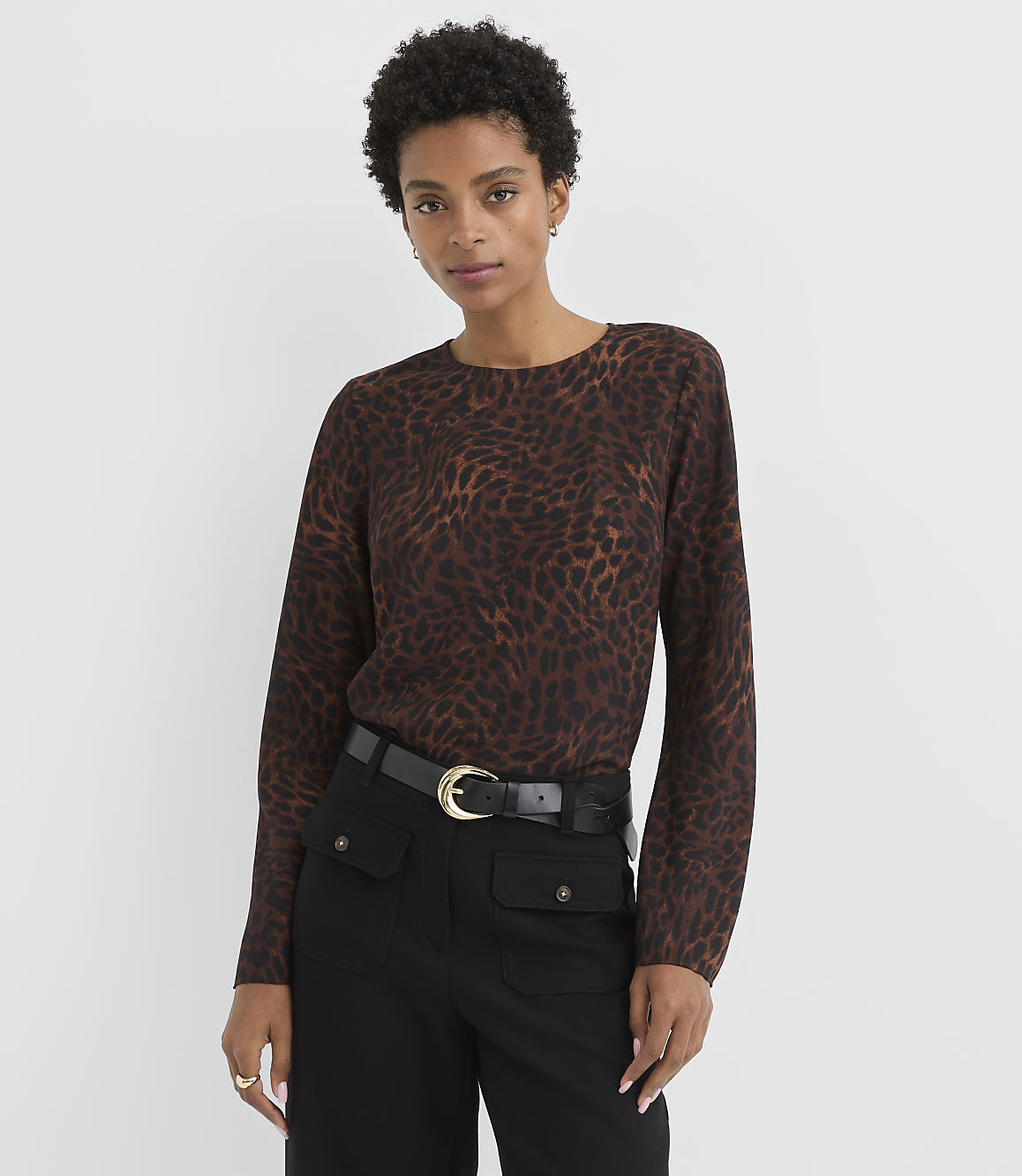 A woman in a brown leopard-print sweater and black pants stands against a plain white background.