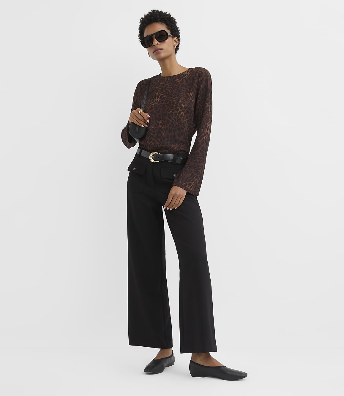 A woman in a leopard print top and black pants stands against a plain white background.