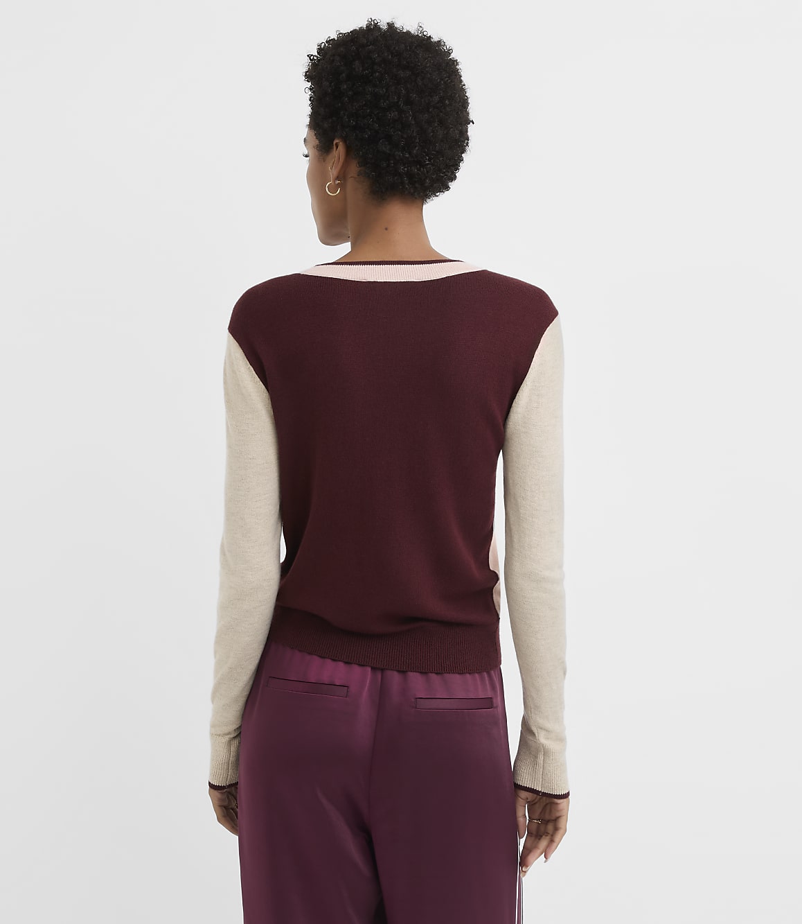 A woman in a maroon and beige sweater and maroon pants stands against a plain white background.