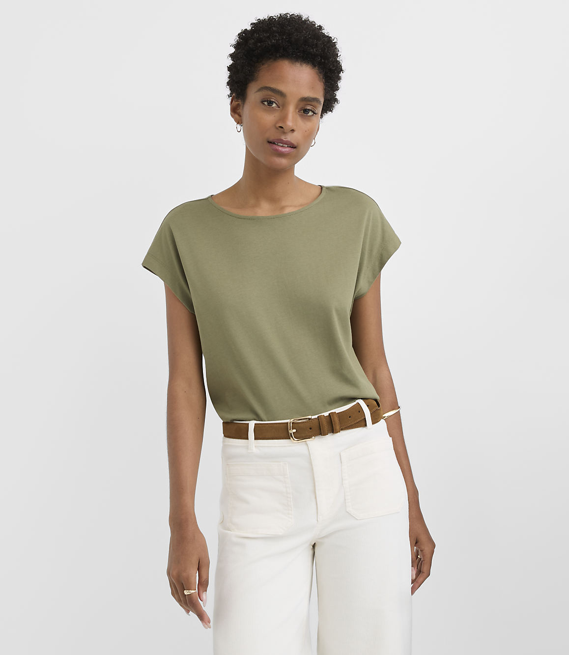 A woman in a green t-shirt and white pants stands against a plain gray background.