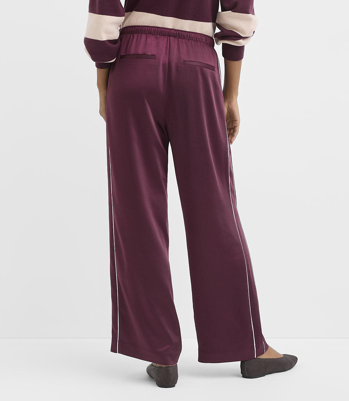 A person wearing burgundy wide-leg pants with white piping stands against a plain white background.