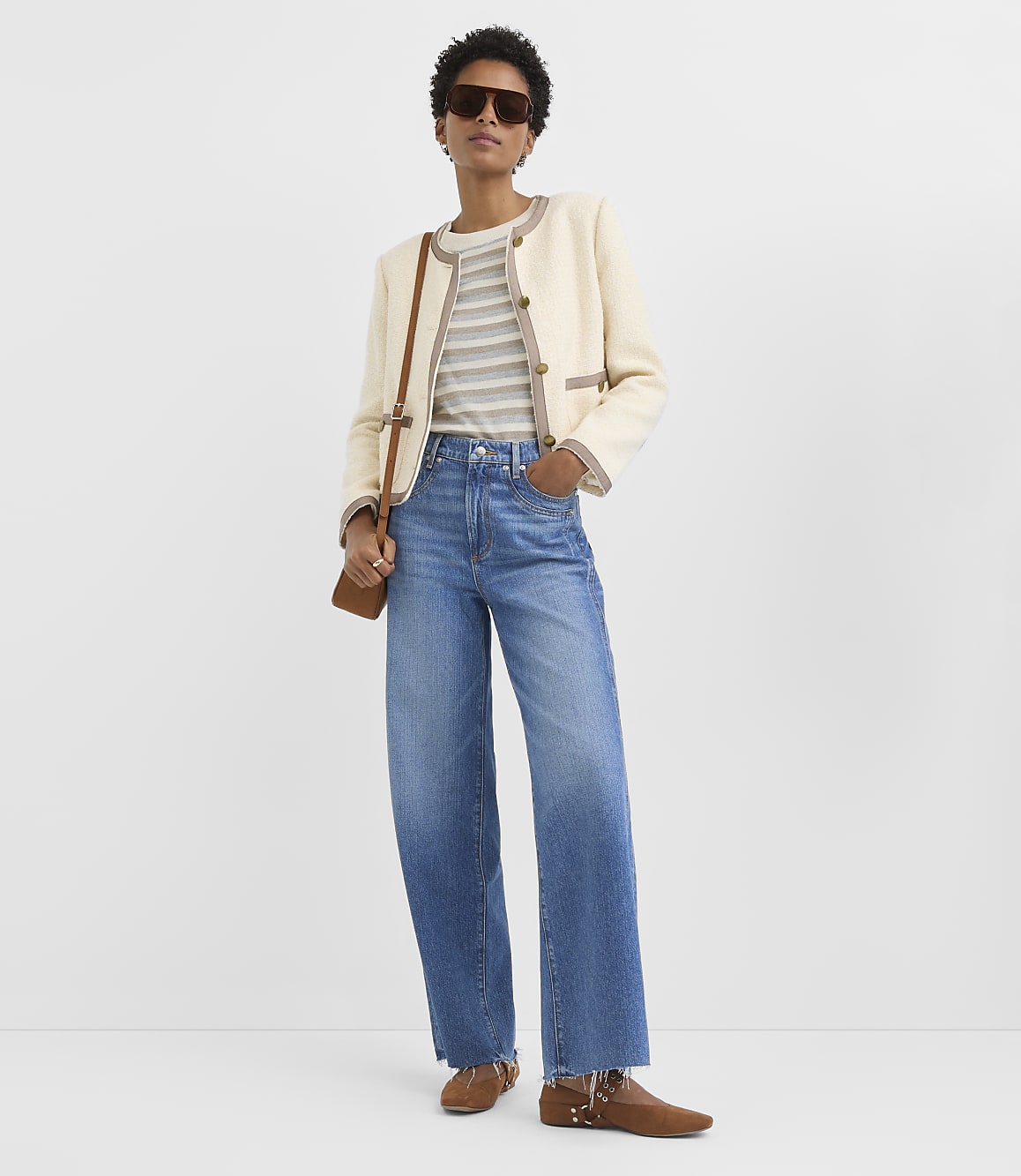 A woman in a cream jacket and striped shirt stands against a plain white background.