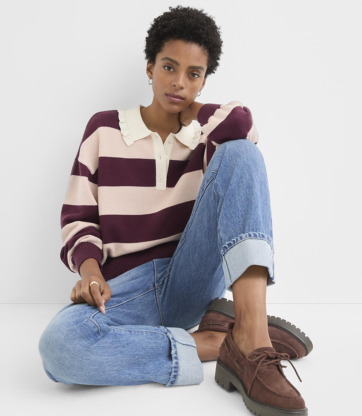 A woman in a striped sweater and cuffed jeans sits against a plain white background.